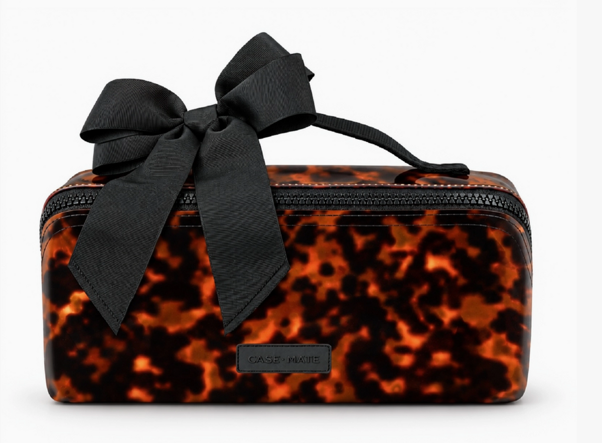 A rectangular cosmetic pouch with a black and orange tortoiseshell pattern, featuring a large black satin bow on top and a small black brand plaque that reads Cashmere.